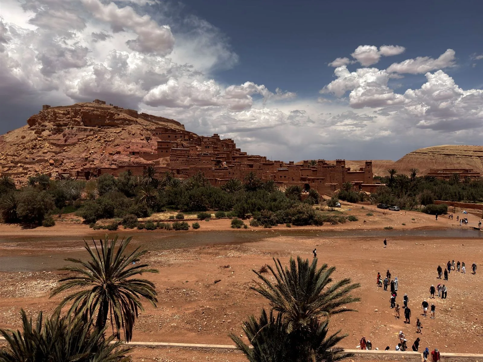 Kasbah de Ait Benhaddou entre palmerales, con cielo de nubes dramáticas en Marruecos.